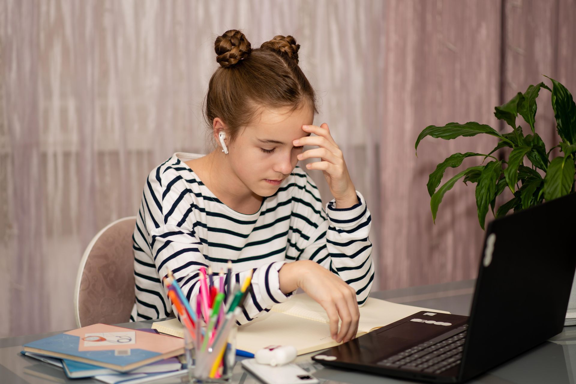 Girl in striped shirt with earbuds, looks stressed at a laptop on a desk.