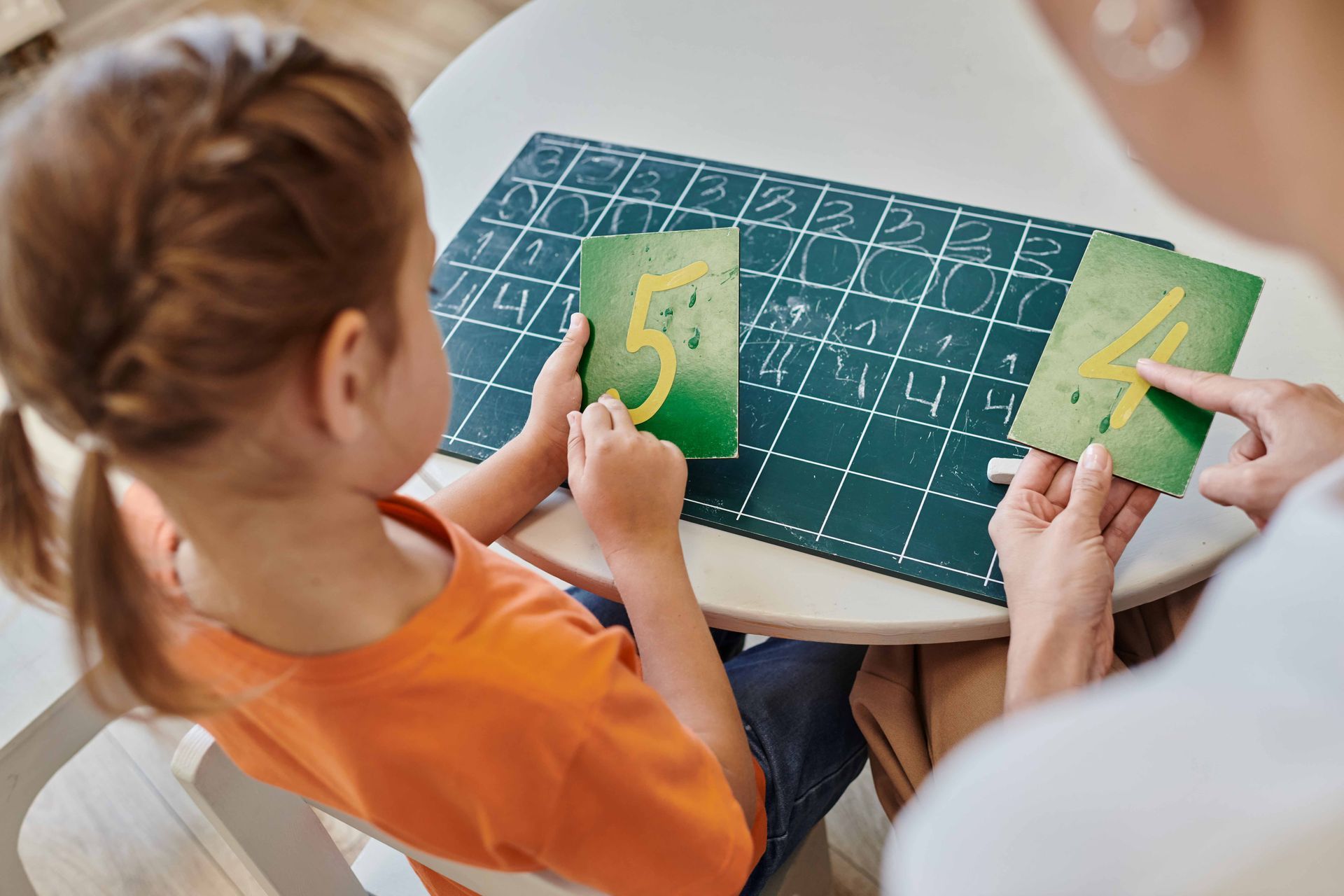 Child learning numbers with help from another person; green cards with numbers 5 and 4.