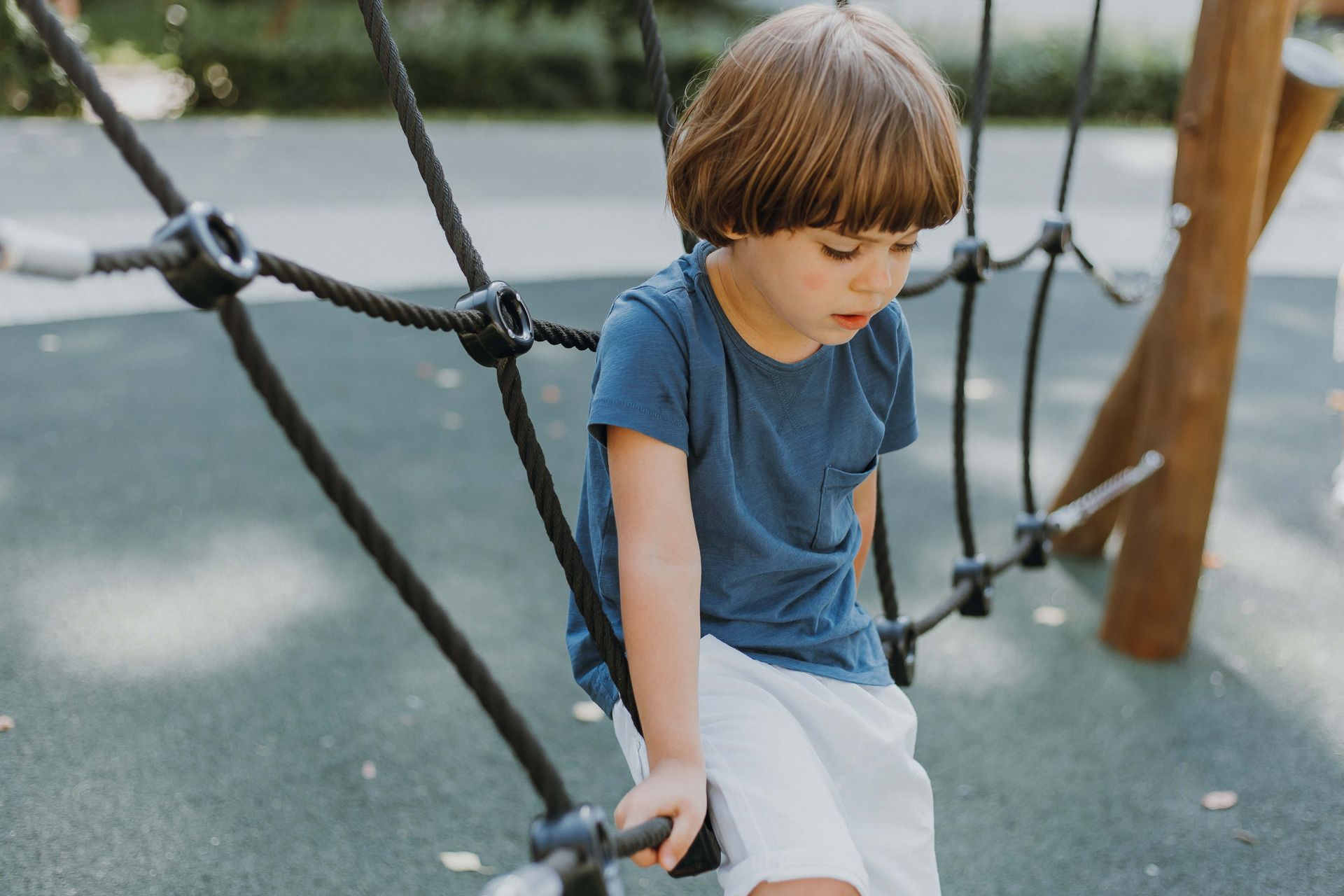 Boy in blue shirt and white shorts on a playground climbing net.