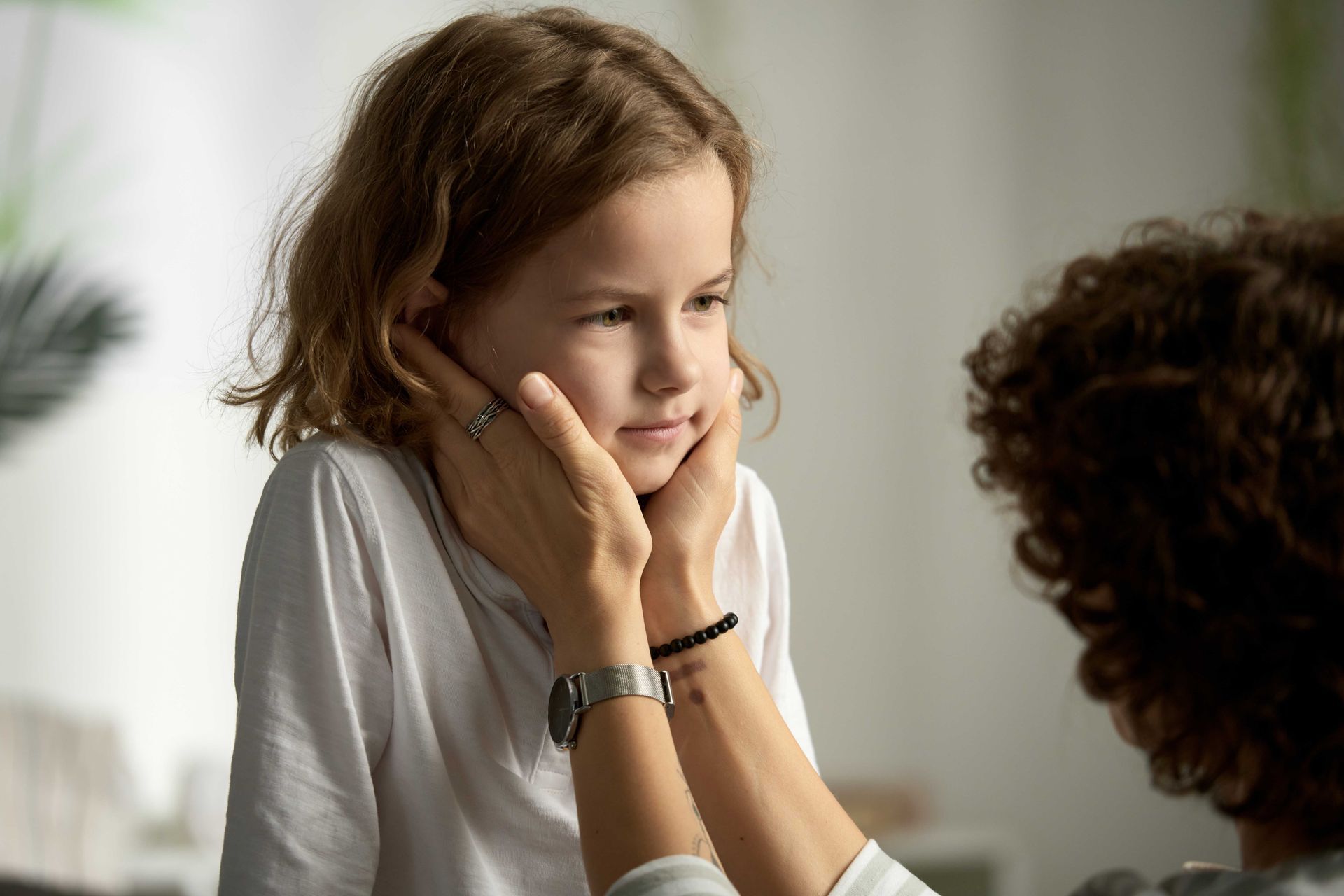 Person's hands gently cupping a child's face; the child appears thoughtful.