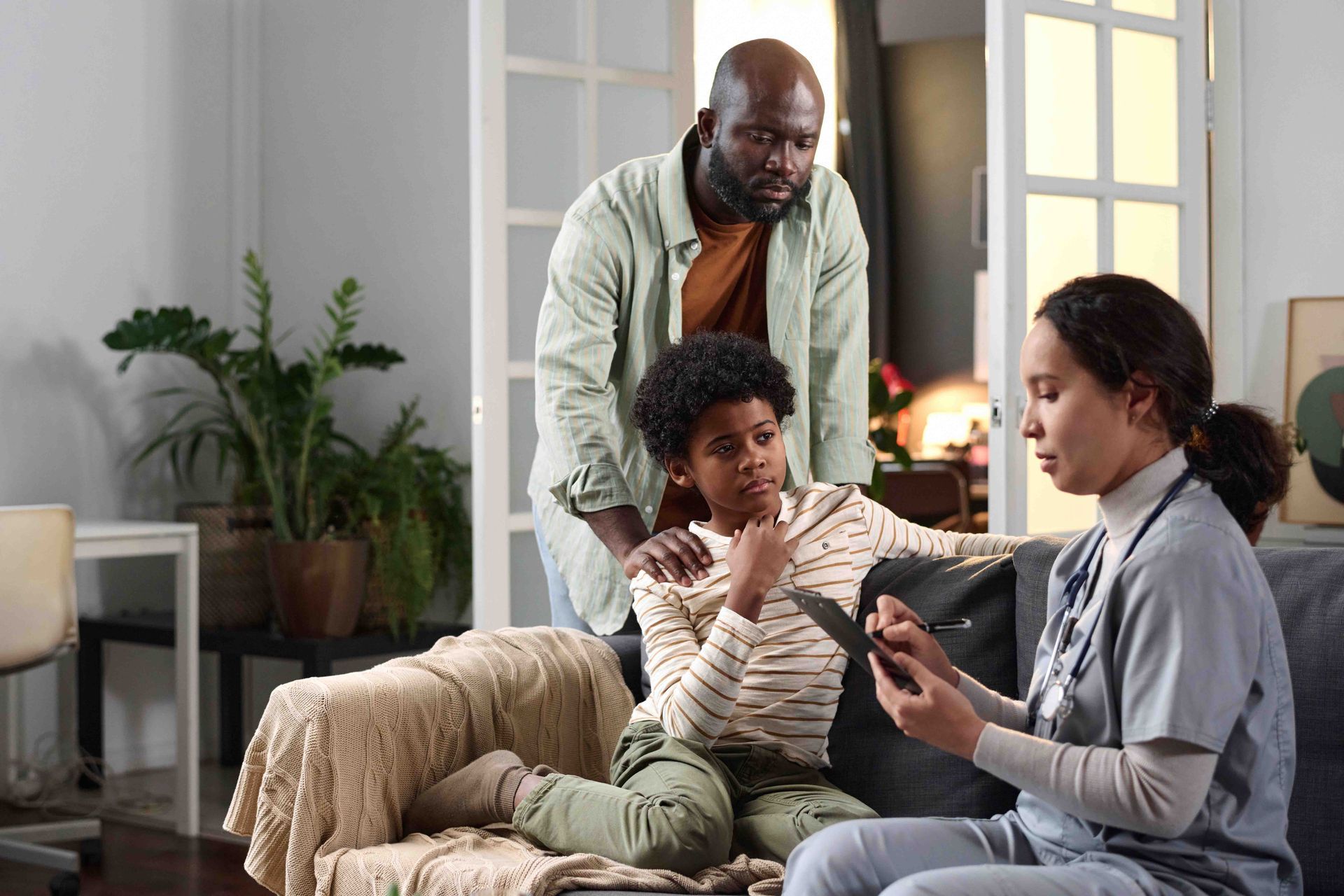 A healthcare worker showing a tablet to a child and parent on a couch.