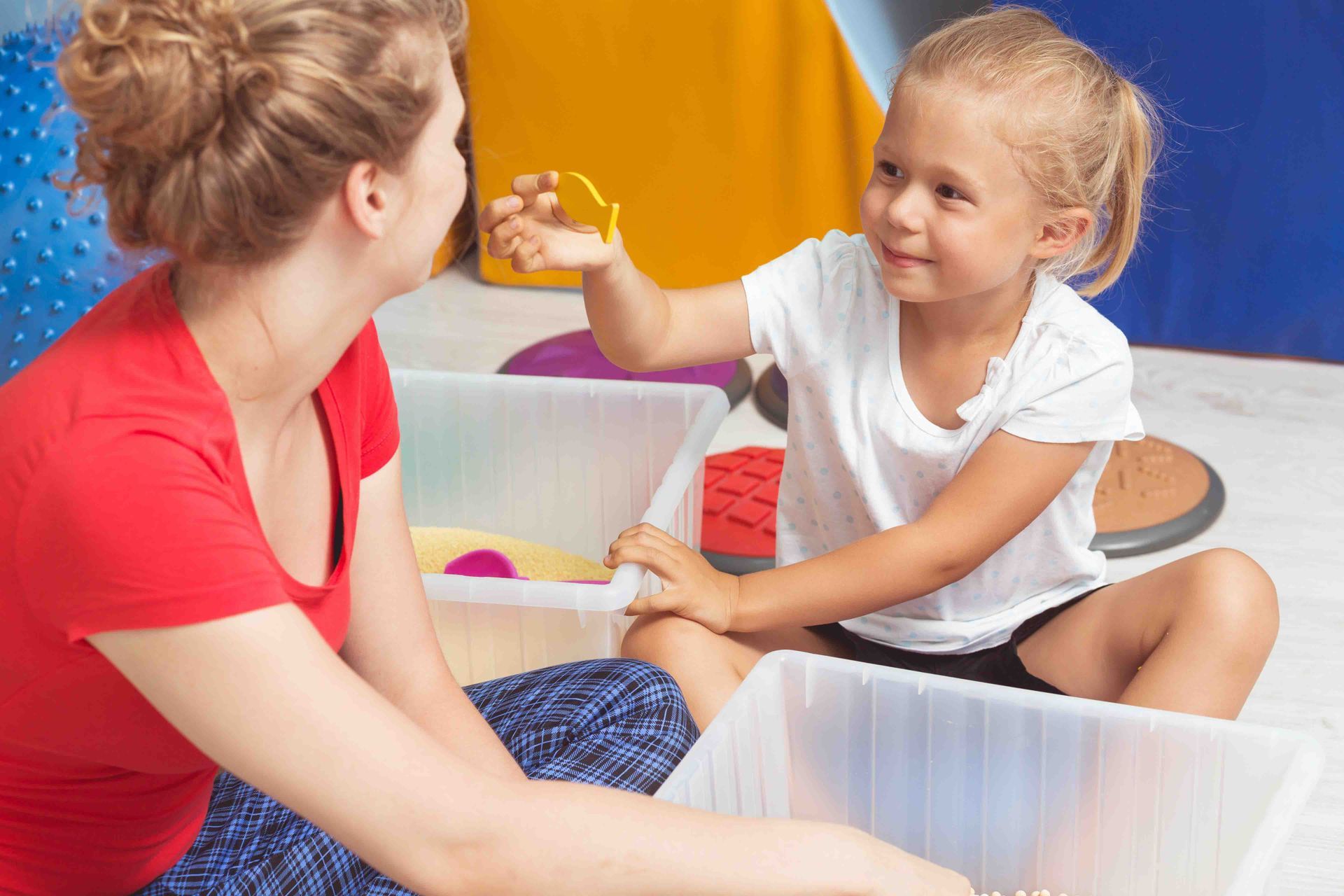 Woman and child sitting, looking at objects in open bins.