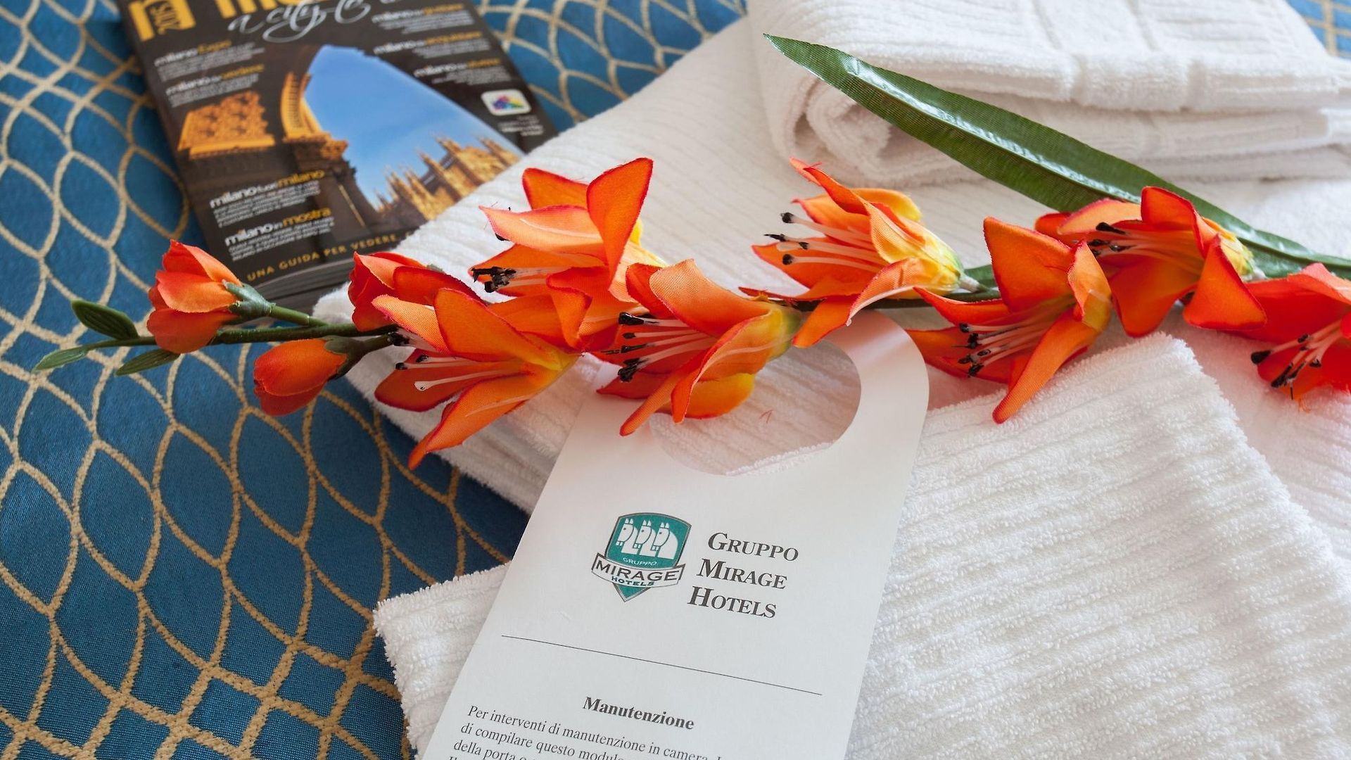 Asciugamani bianchi, fiori arancioni, appendiabiti da porta d'albergo su una superficie con motivi blu.