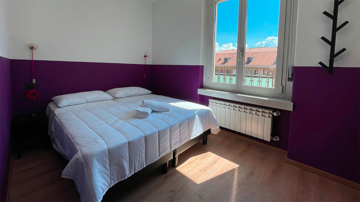 Camera da letto con letto matrimoniale, pareti viola e finestra con vista.