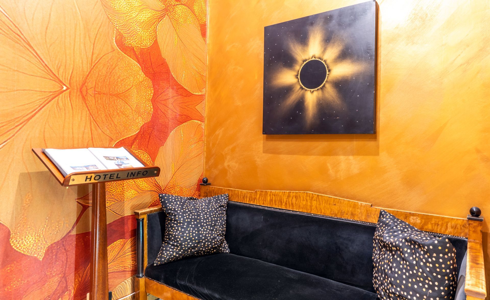 Camera nei toni dell'arancione con divano in velluto nero, cuscini decorativi, opere d'arte e un supporto in legno