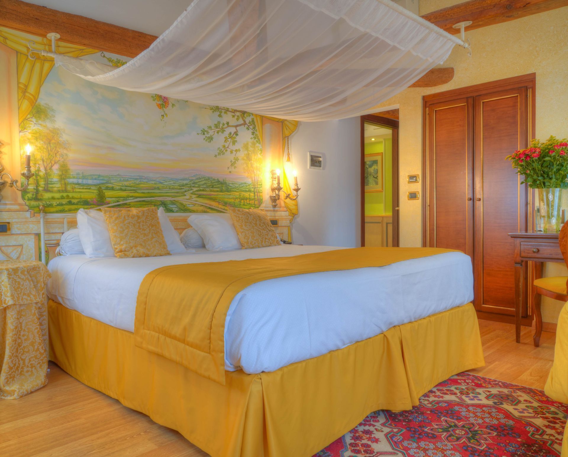 Accogliente camera d'albergo con copriletto giallo, baldacchino, murale e tappeto floreale.