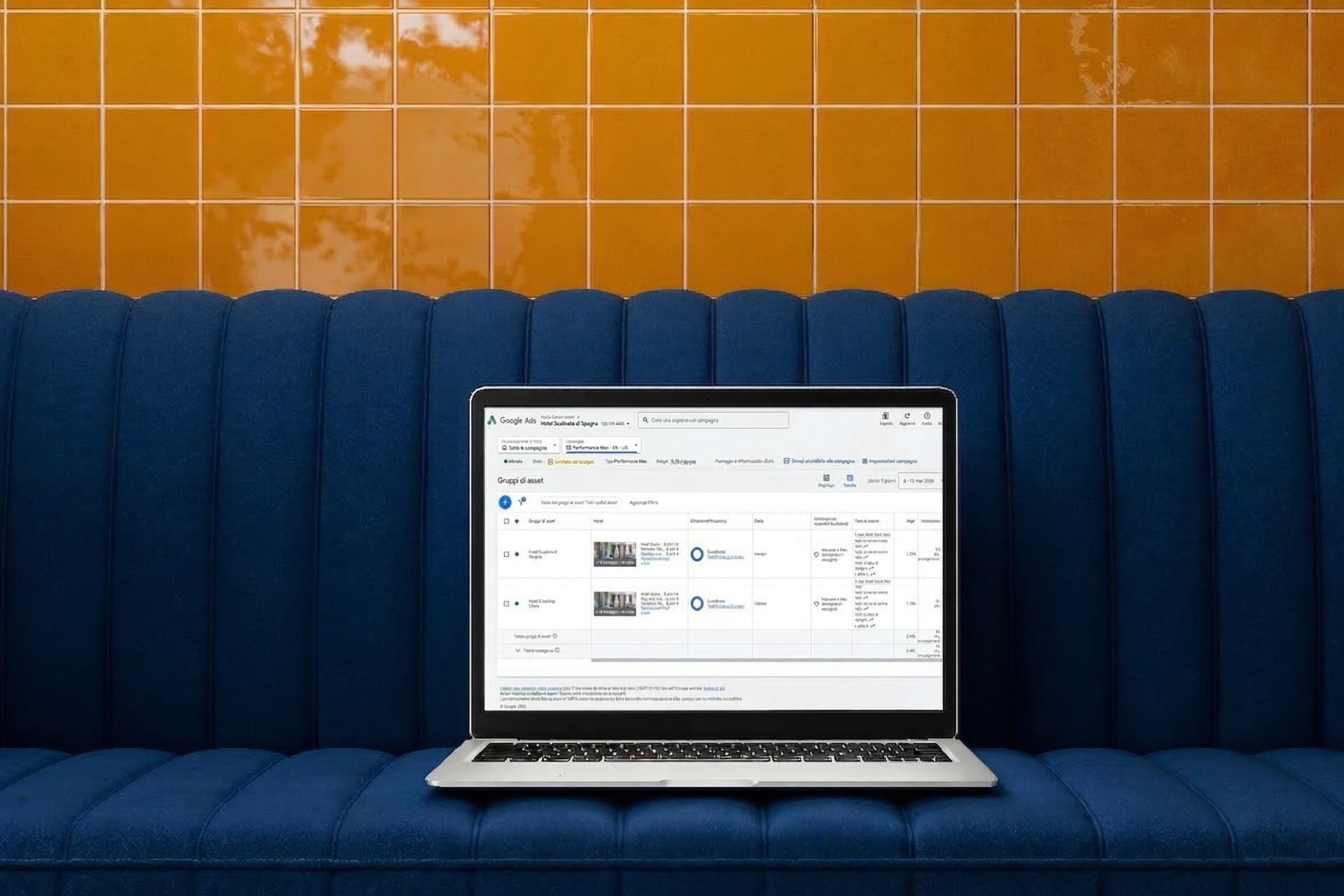 A laptop displaying a dashboard perfromance max hotel on a blue ribbed sofa in front of a yellow tiled wall.