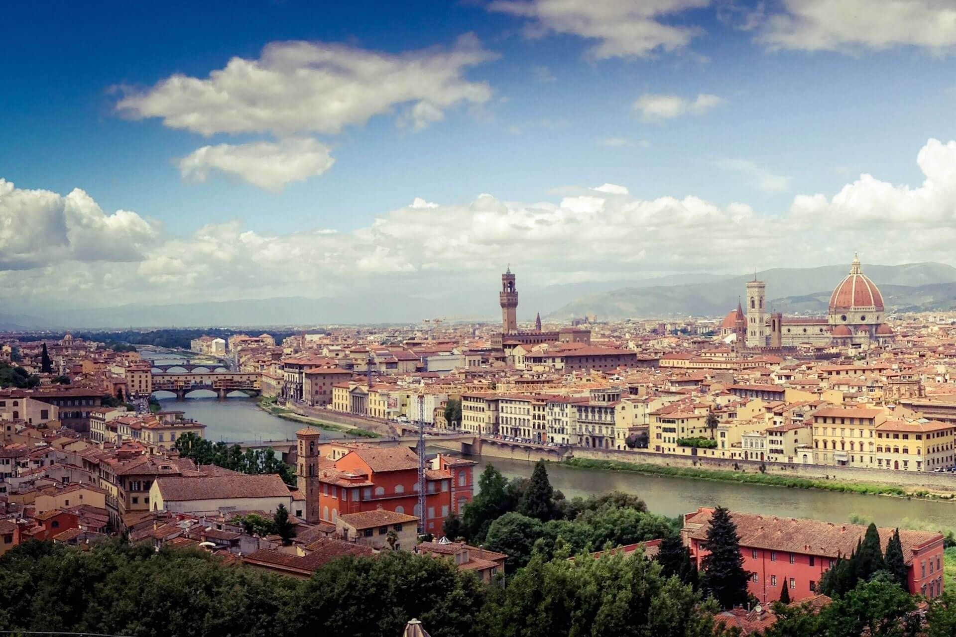 Paesaggio urbano di Firenze, Italia, con fiume, ponti e l'iconico Duomo sotto il cielo azzurro.