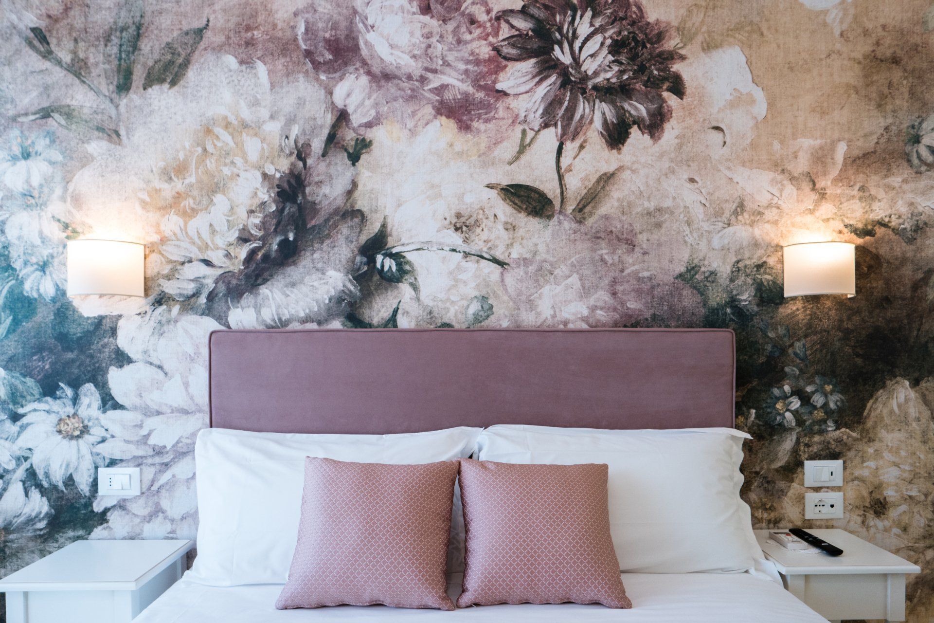 Camera da letto con carta da parati floreale, letto con cuscini rosa e applique.