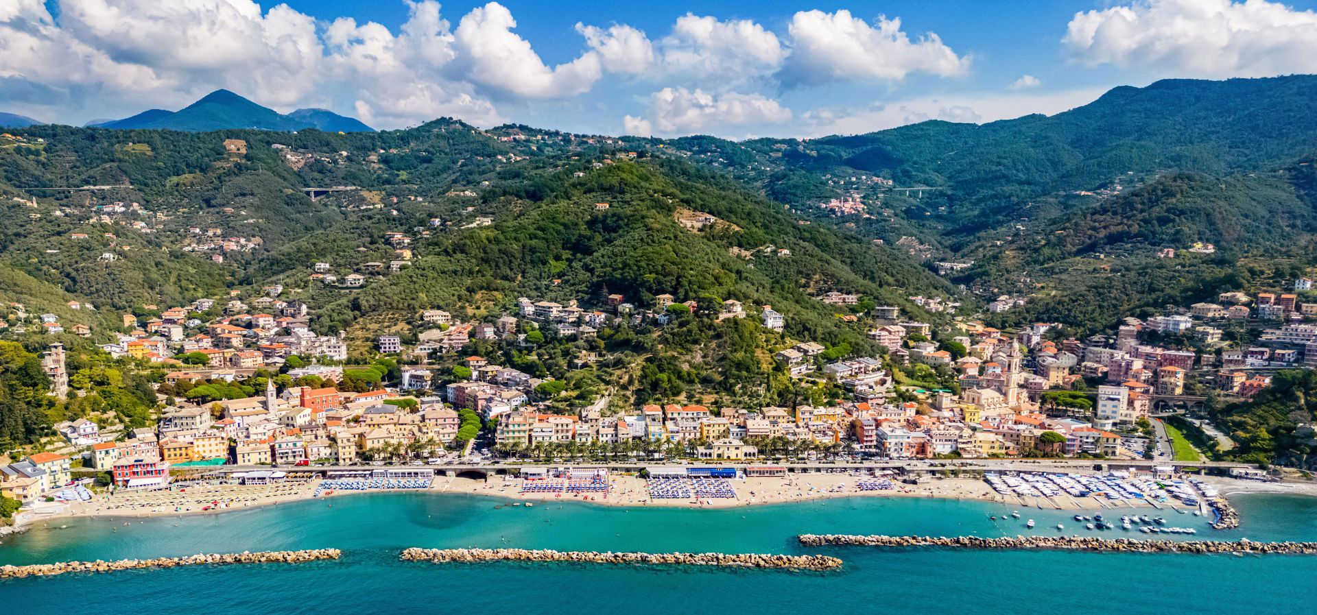 Città costiera con edifici colorati, circondata da montagne e acque turchesi.