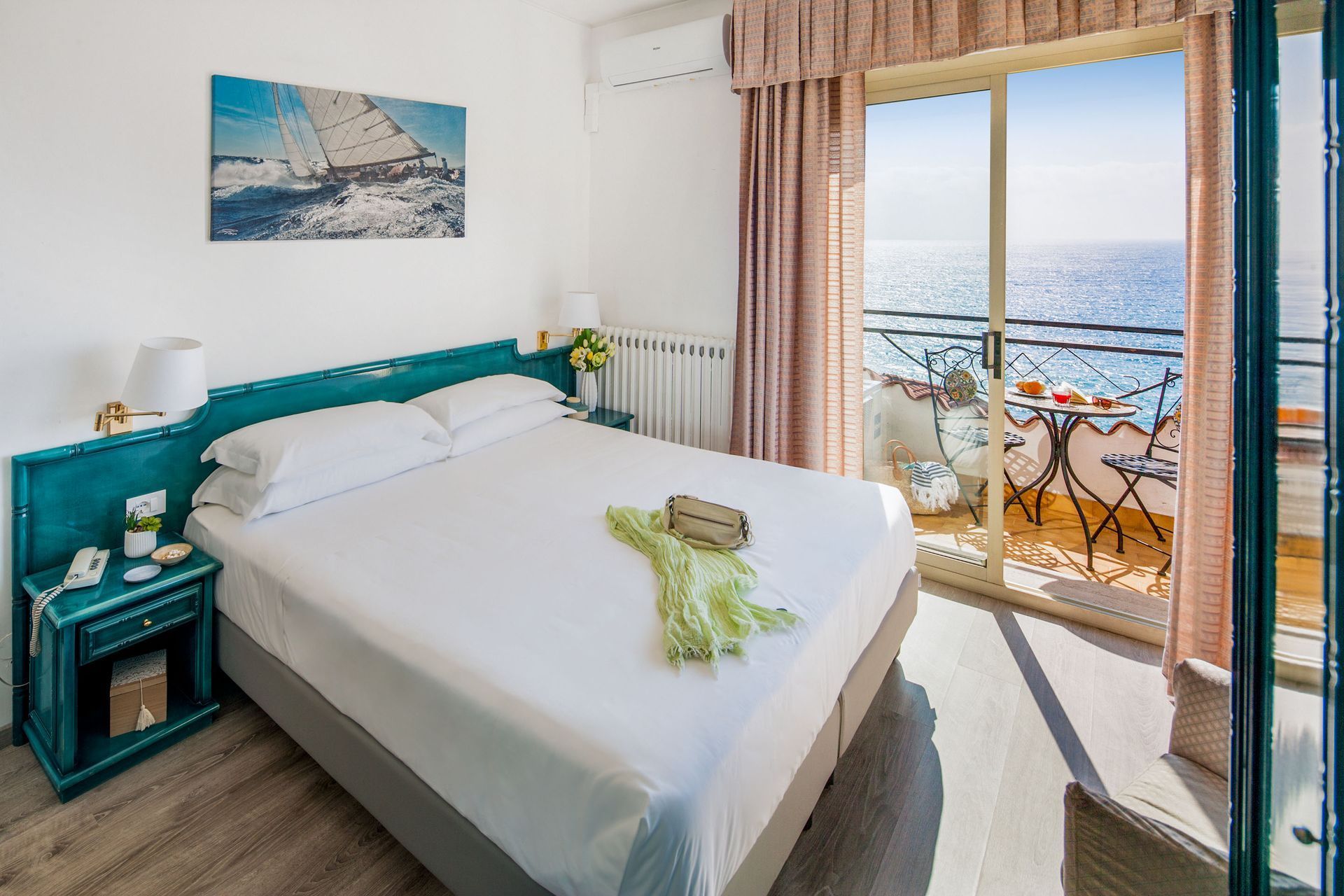 Camera da letto con letto, balcone con vista sul mare, colori azzurro e crema.