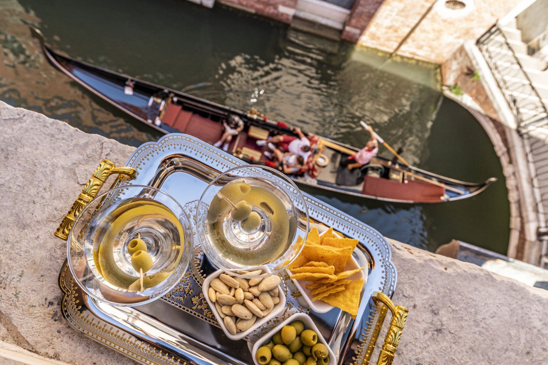 Vassoio d'argento con bevande e snack con vista su un canale veneziano con gondola.