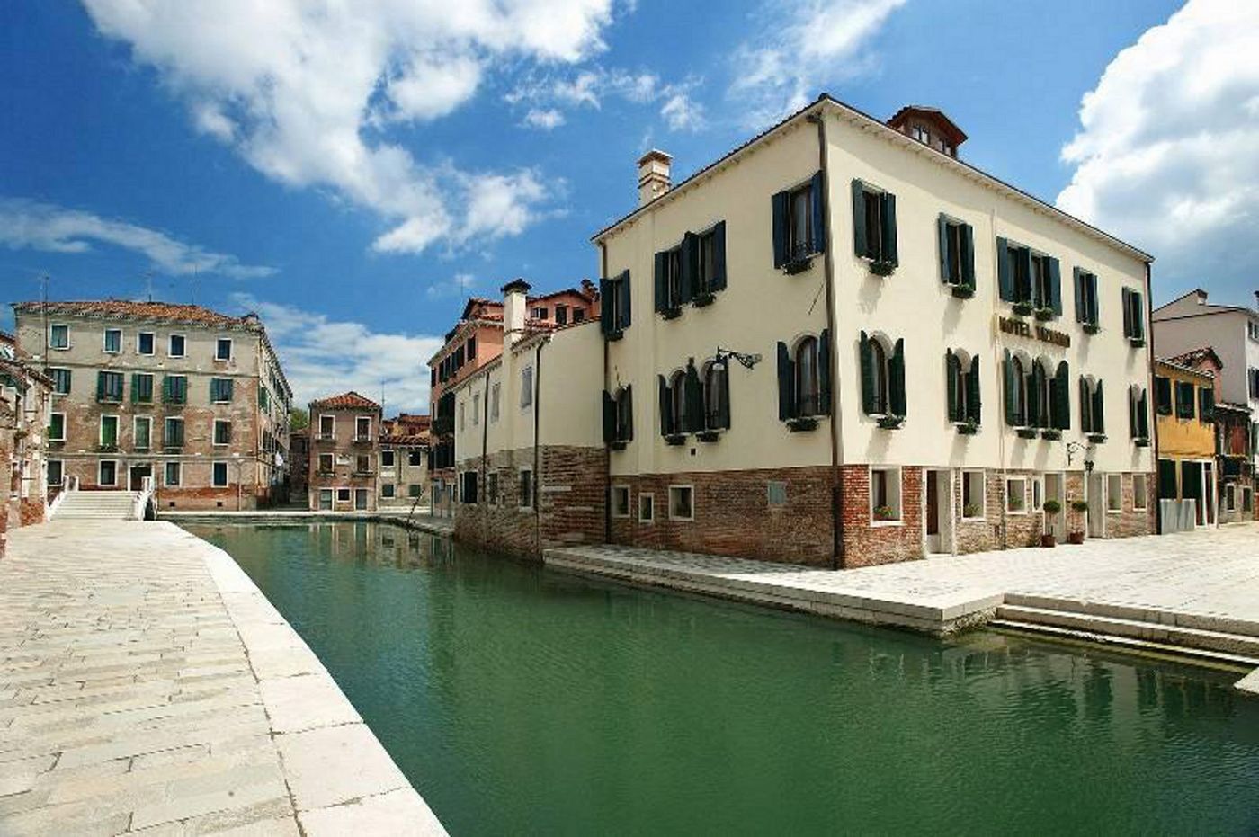 Canale di Venezia con edifici su entrambi i lati, acqua al centro, cielo azzurro con nuvole in alto.