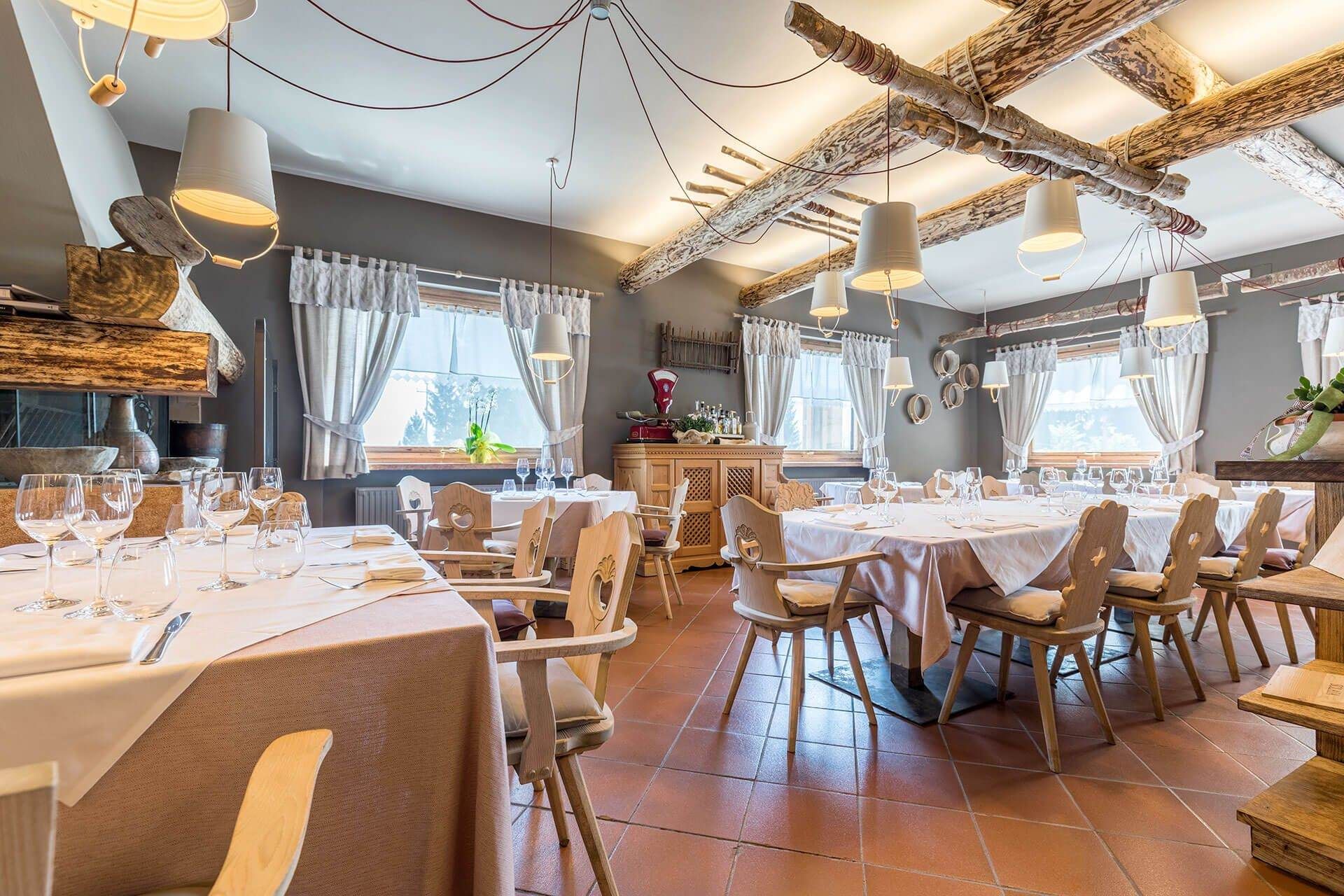 Interno del ristorante: tavoli apparecchiati con tovaglie bianche, sedie in legno e lampade.