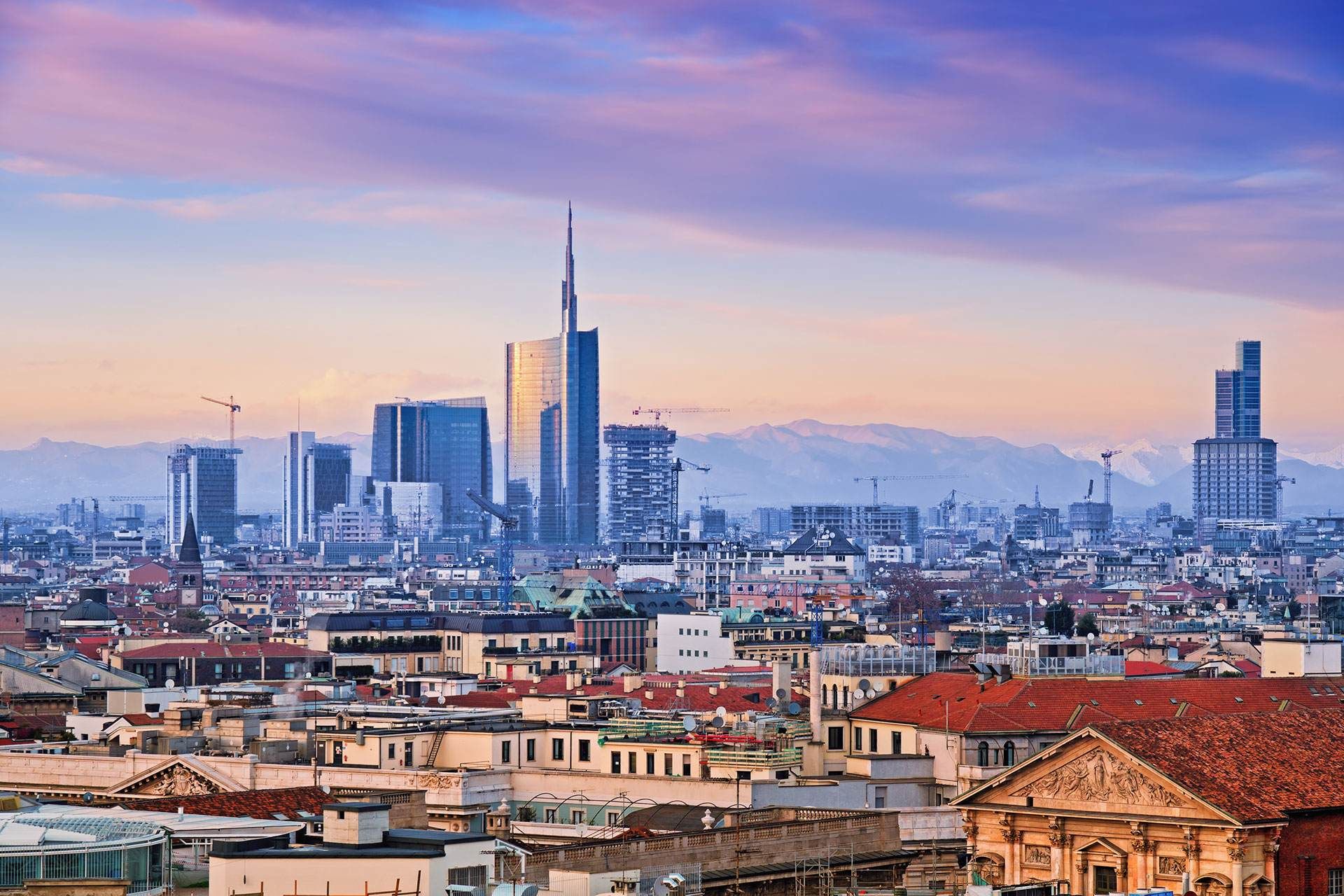 Skyline di Milano al tramonto: grattacieli e palazzi sotto un cielo color pastello.