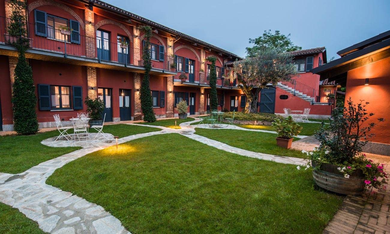 Edificio rosso con finestre ad arco, un sentiero in pietra e un cortile verde.