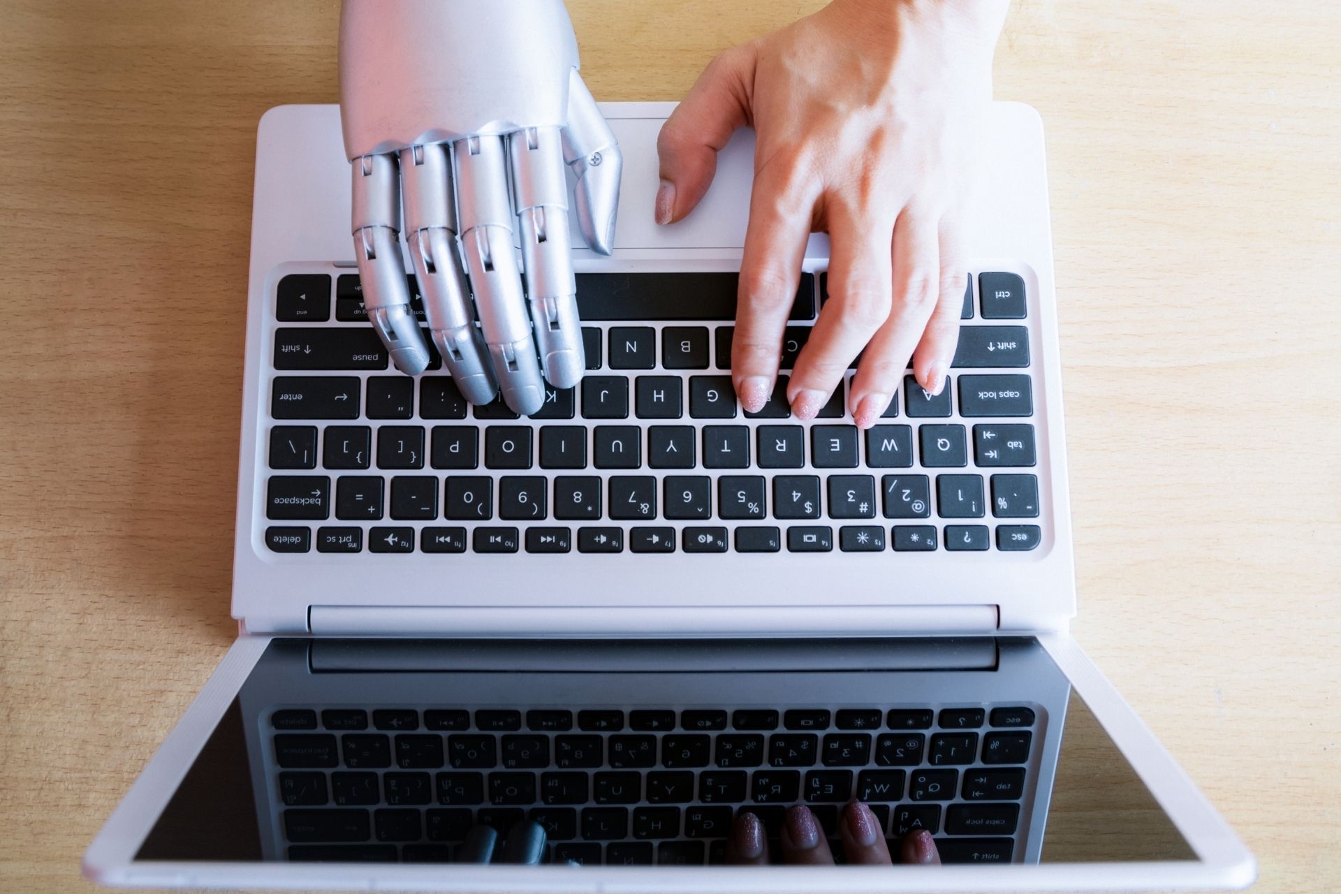Mano robotica e mano umana che digitano su un computer portatile.