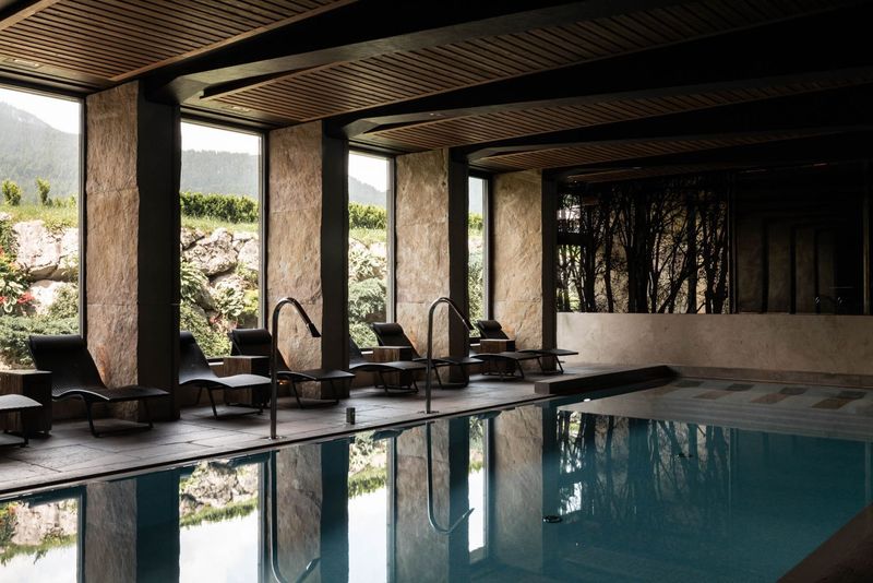 Piscina coperta con sedie a sdraio, ampie finestre e vista sulle montagne.