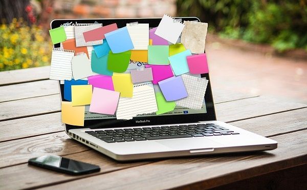 Un computer portatile ricoperto di post-it colorati, appoggiato su un tavolo di legno con un telefono nelle vicinanze.