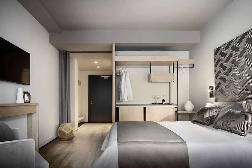 Interno di una camera d'albergo con letto, TV, armadio e porta; colori neutri, design moderno.