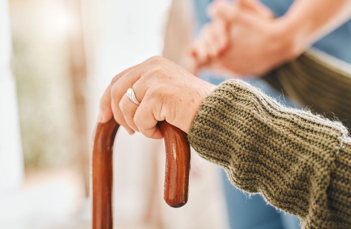 Hand holding a wooden cane, with another person assisting in the background