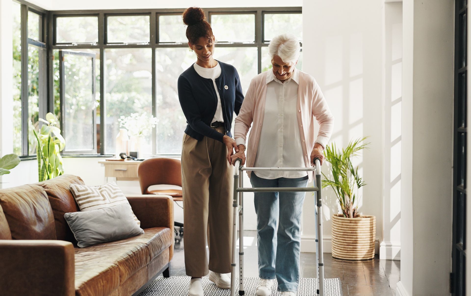 Caregiver assisting elderly woman with walker in a bright living room