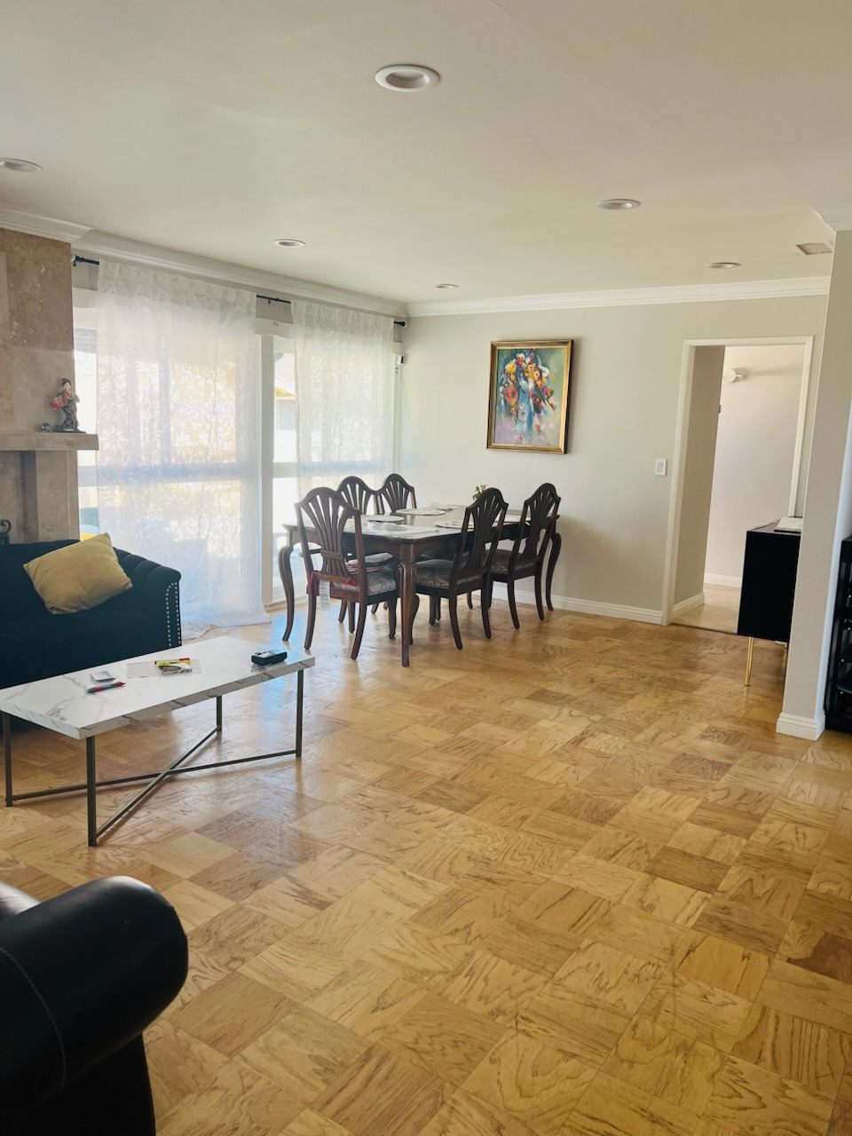 Bright living-dining room with parquet floor, glass coffee table, dark sofa, and wooden dining table near windows.