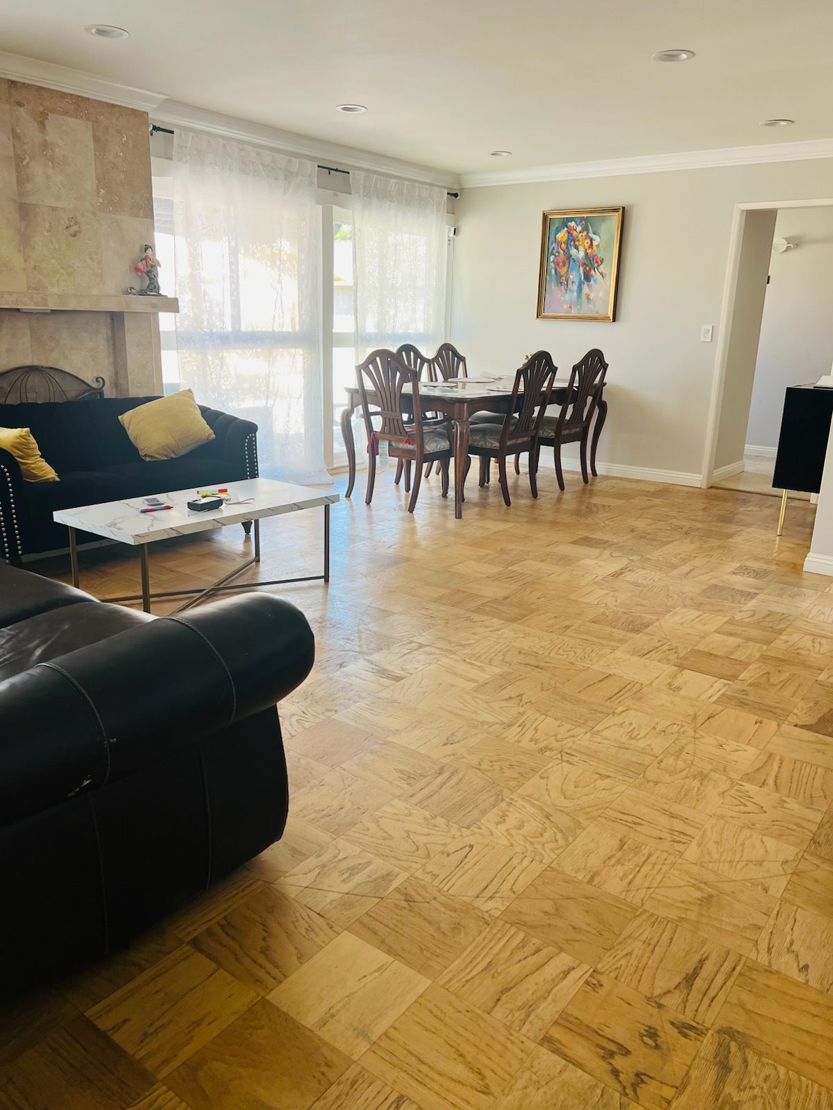 Bright living room with black sofa, coffee table, dining set, large windows, and parquet floor