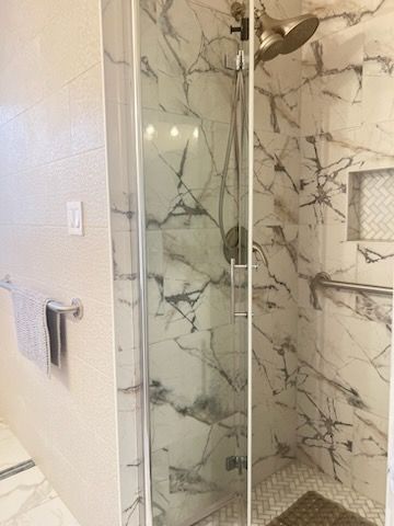 Modern bathroom shower with marble-pattern tile, glass door, and wall-mounted towel rack