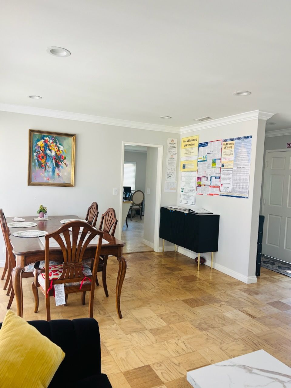 Bright dining room with wooden table and chairs, colorful wall art, and a bulletin board in the background