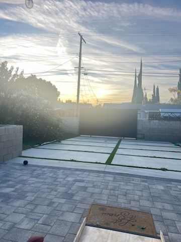 Sunlit paved patio with low walls, a covered grill, and a cloudy sky at sunset