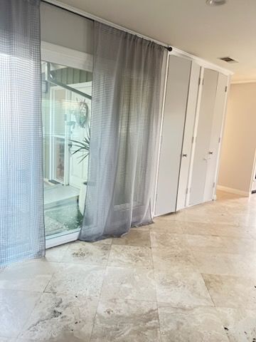 Bright modern room with marble floor, sheer gray curtains, and white closet doors by a sliding glass window