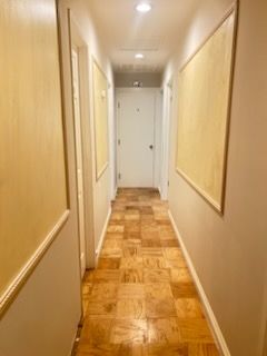 Narrow hallway with light wood flooring, beige walls, and closed white doors at the end.