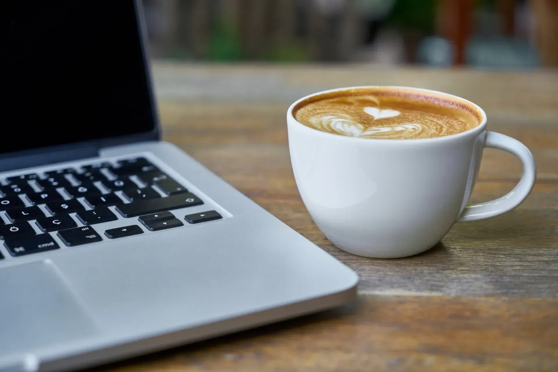Computadora portátil y taza de café blanco con arte latte sobre una mesa de madera.