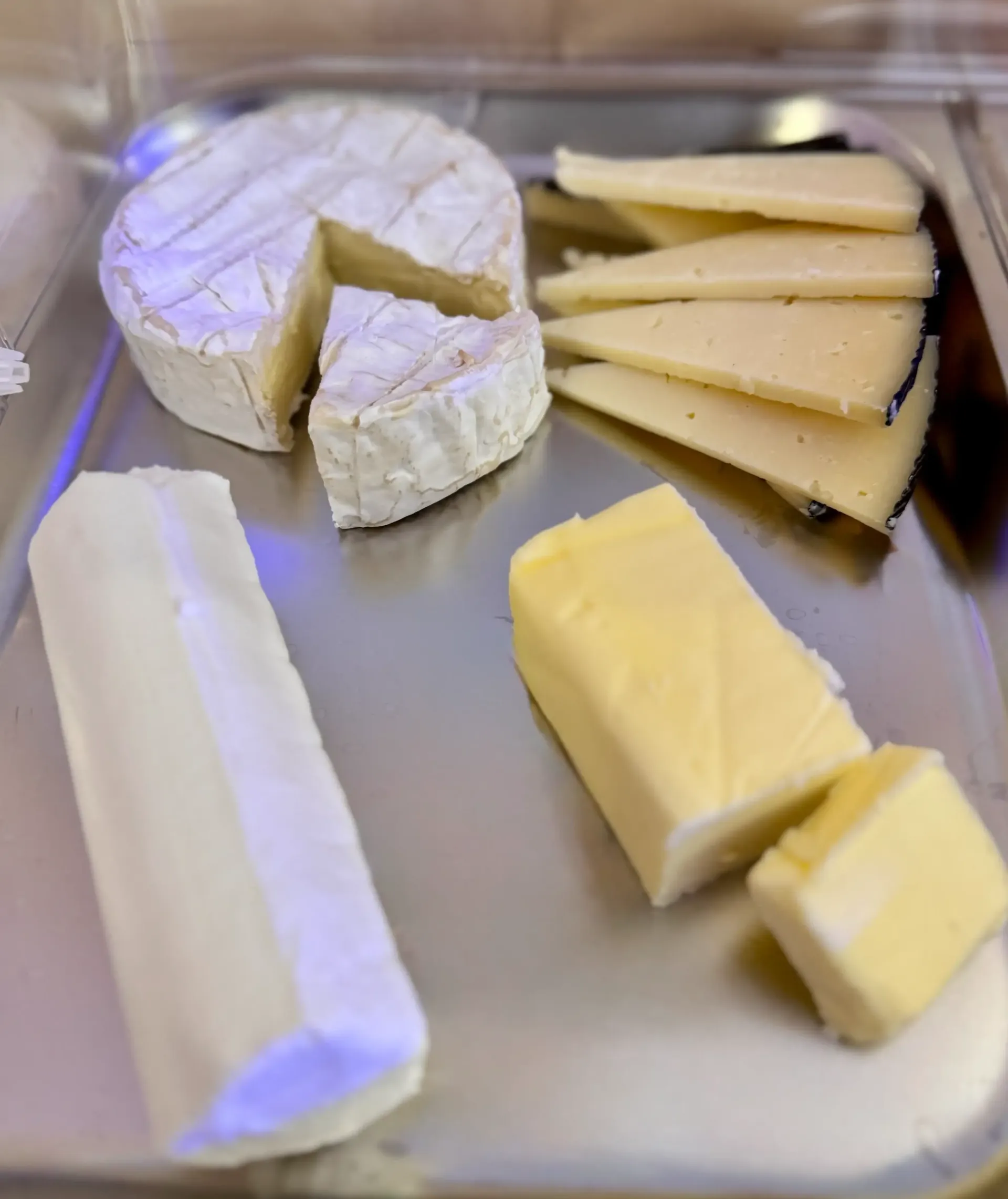 Una bandeja plateada con queso brie, queso curado en lonchas, un trozo de queso de cabra y dos bloques de mantequilla.
