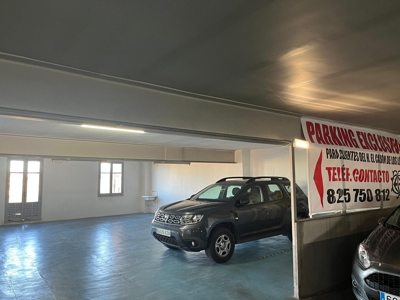 Un aparcamiento cubierto con un coche oscuro estacionado en el centro y un cartel de contacto colgado en el lado derecho.
