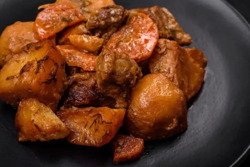 Una ración de estofado de ternera con trozos grandes de patatas y zanahorias en un plato negro.