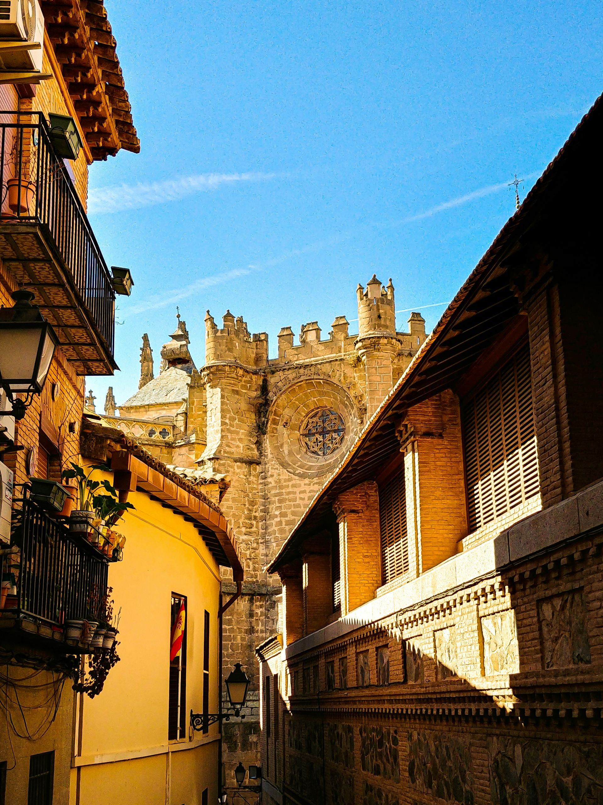 Una calle estrecha con un edificio amarillo a la izquierda y un muro de piedra a la derecha, que enmarcan la vista de una gran catedral.