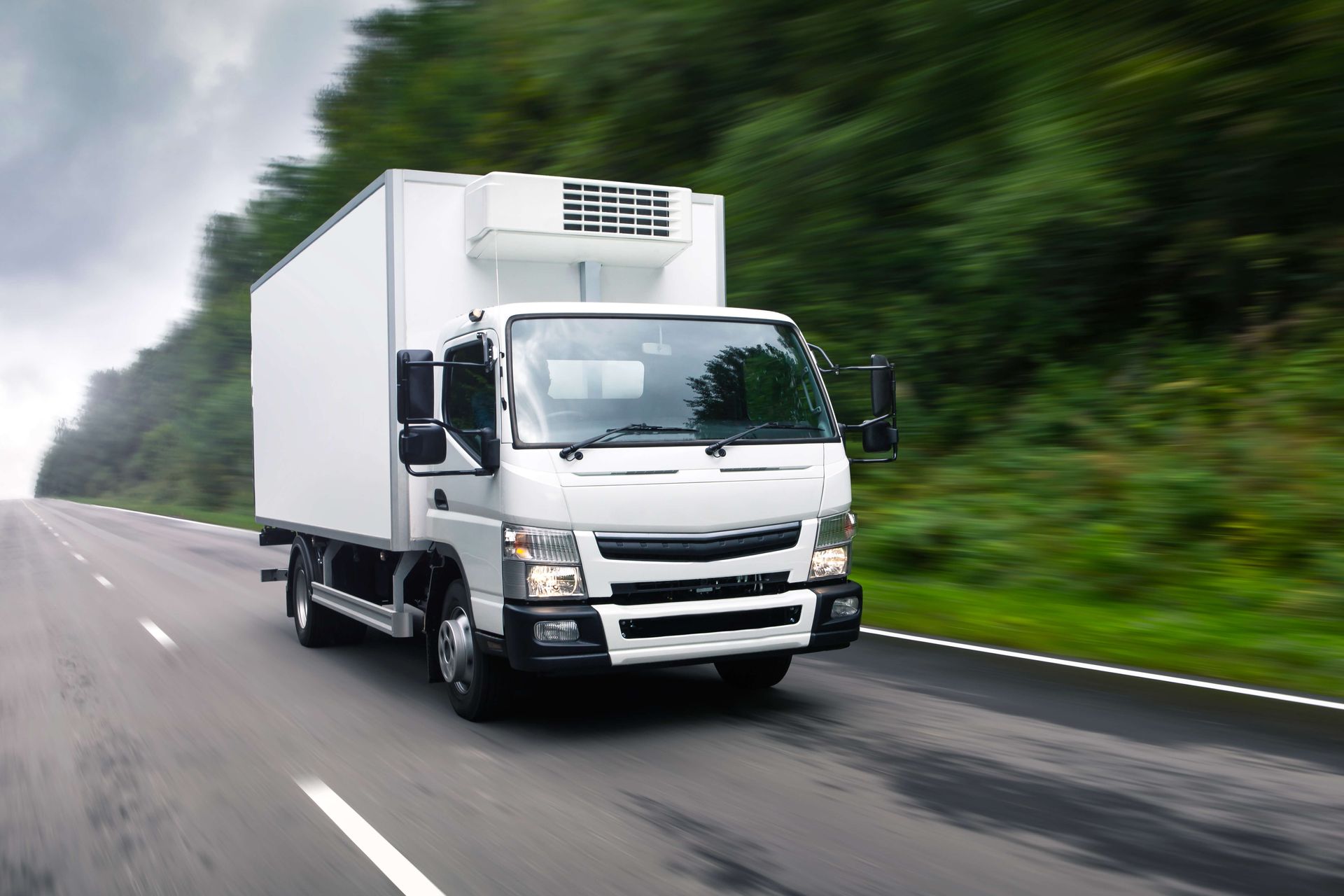 White box truck driving on a wet highway beside green trees