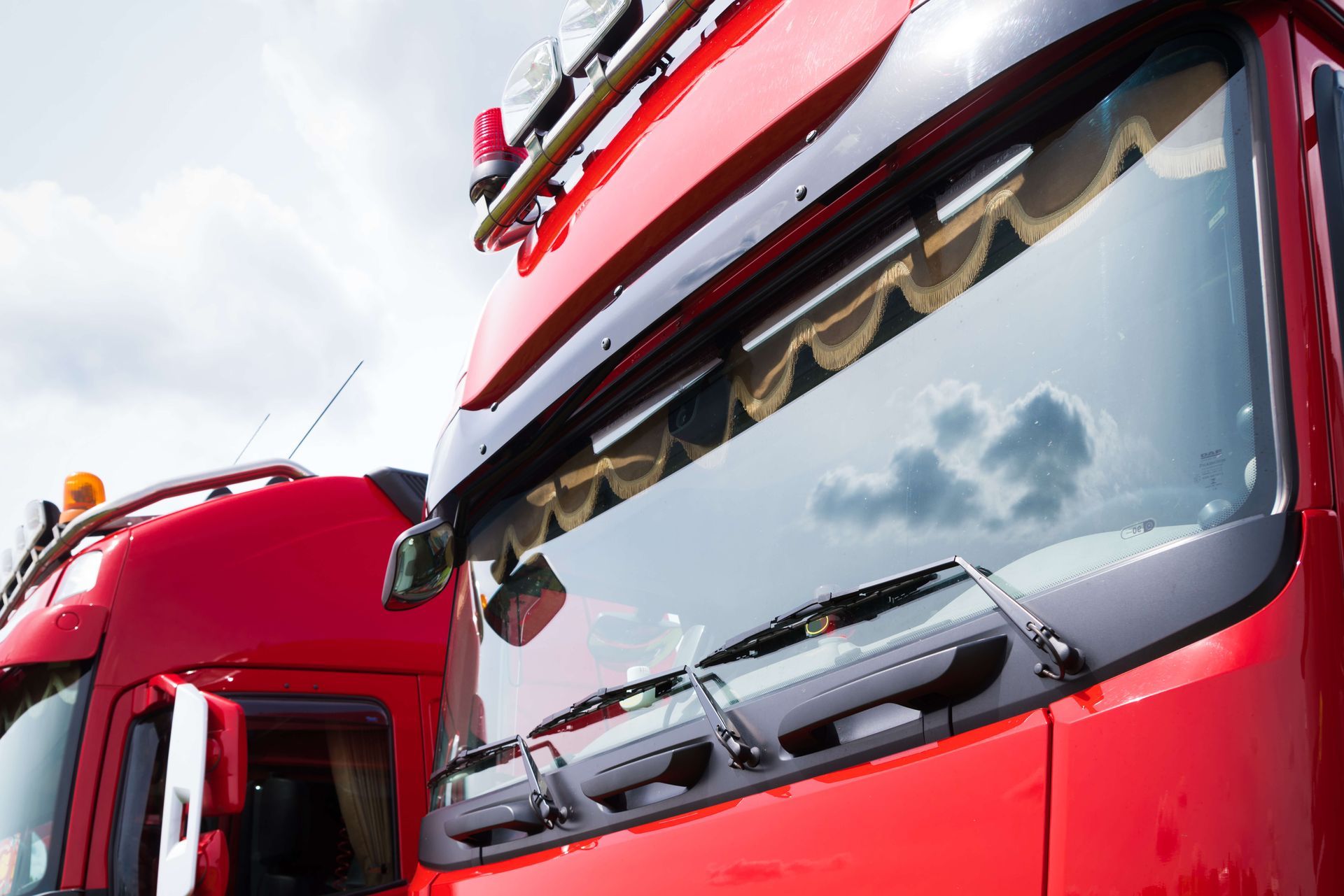 Close-up of two red fire trucks with windshields and roof equipment against a cloudy sky