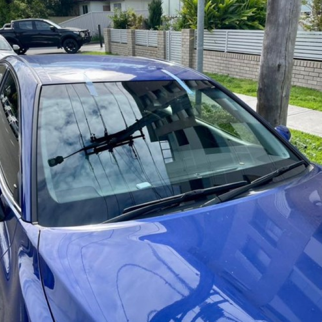 Blue car parked on a sunny street with power lines reflected in the windshield