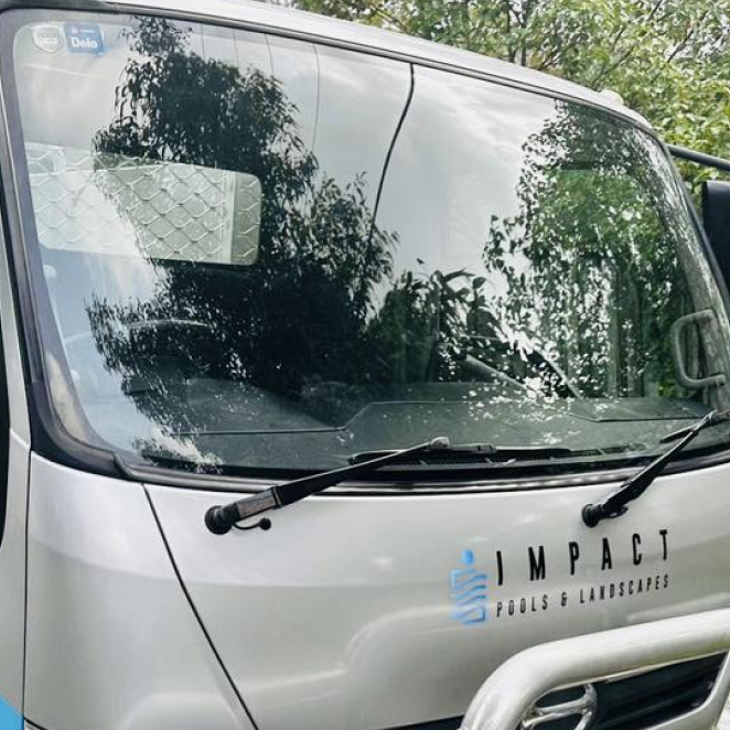 White van windshield with reflections of trees and the “Impact” logo on the hood