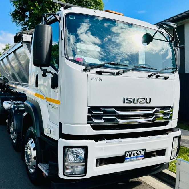 White Isuzu dump truck parked on a roadside under a blue sky