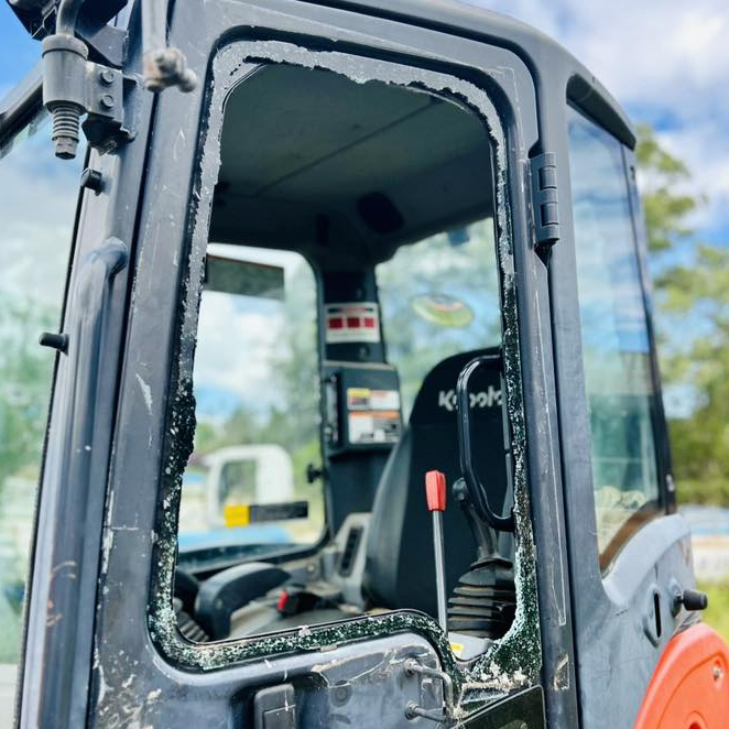 Close-up of a black construction cab with a cracked window and orange trim under a blue sky