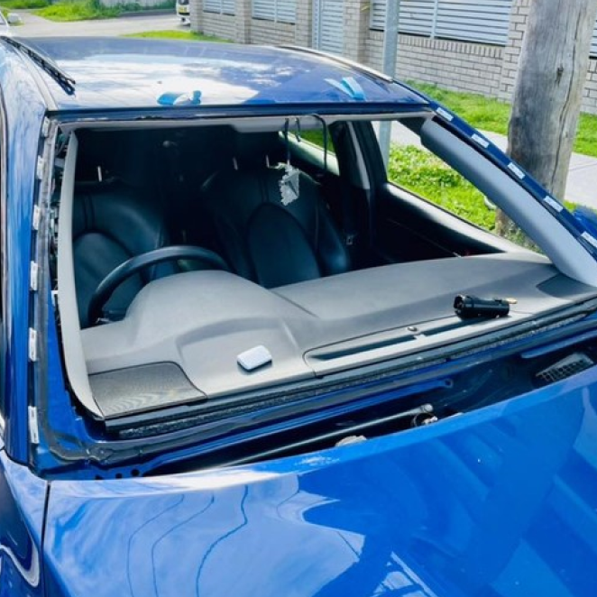 Blue car with shattered windshield and damaged roof, parked outdoors.