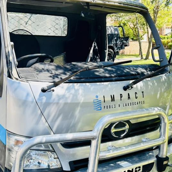 White Impact truck with logo on front, parked outdoors with windshield damaged or missing.