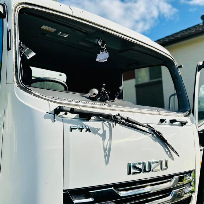 Damaged white Isuzu truck with smashed windshield and bent front panel under a blue sky