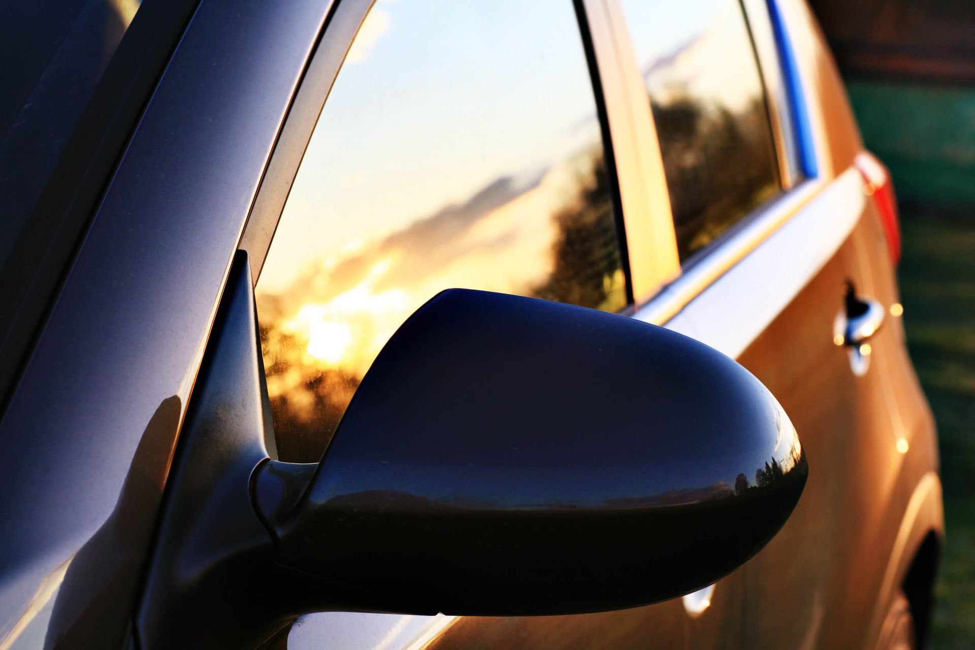 Close-up of a car’s black side mirror on a brown vehicle at sunset