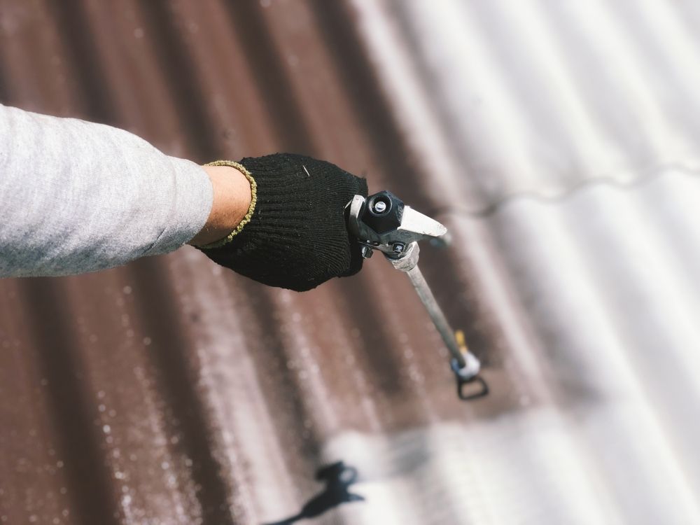 Person In Black Glove Sprays White Paint On Brown Corrugated Metal Roof — TMP Painting Services in Beaconsfield, QLD