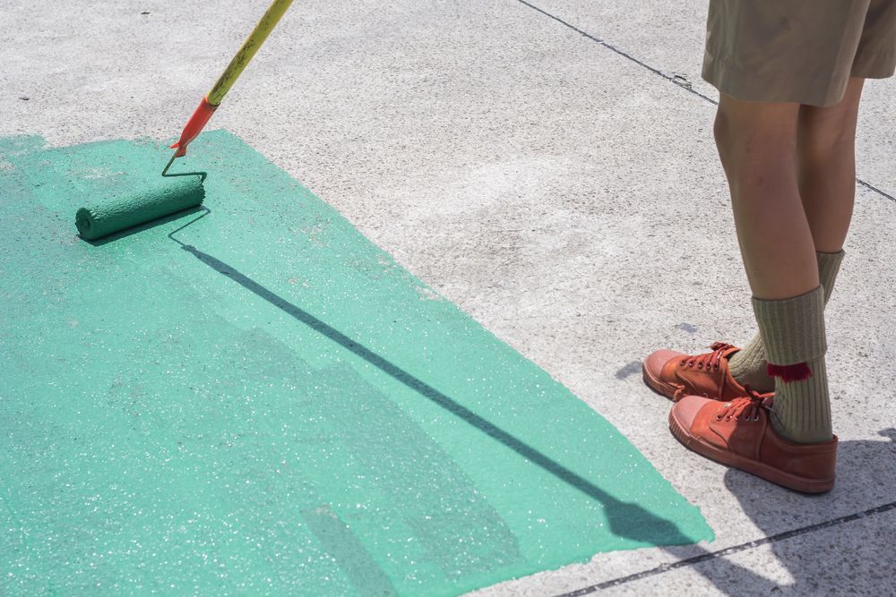A Person Painting A Concrete Surface With A Green Roller; Setting Is Outdoors — TMP Painting Services in Beaconsfield, QLD